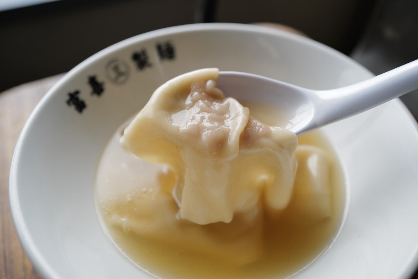白いレンゲにのせたワンタン。透き通ったスープの「富喜㊂製麺」の丼。